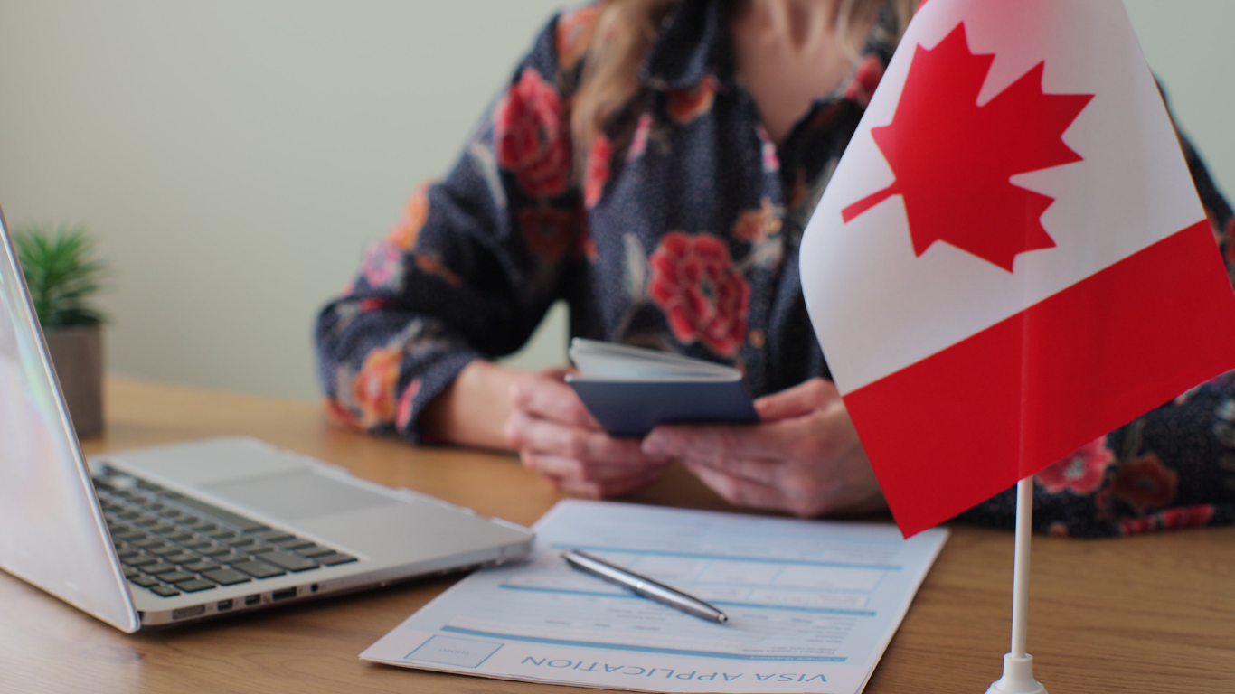 Person holding a passport beside a Canadian flag and visa application forms